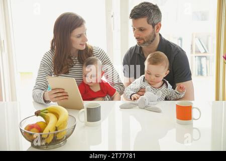 Coppia seduta a tavola con Baby gemelli con tavoletta digitale Foto Stock