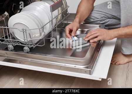 bell'uomo che mette una compressa di detergente in lavastoviglie in cucina Foto Stock