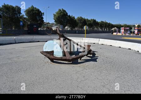 Vecchia ancora arrugginita con catena posta al centro della rotonda con segnaletica stradale e barriera in cemento in città- Foto Stock