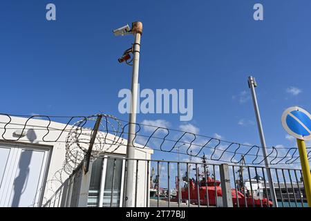 Il filo spinato sulla parte superiore della recinzione e le telecamere a circuito chiuso all'ingresso del bacino passeggeri. Foto Stock