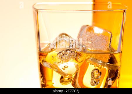 dettaglio di un bicchiere di bevanda come whisky con ghiaccio su sfondo caldo e chiaro Foto Stock