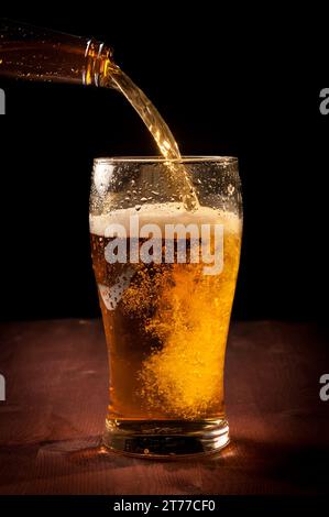 birra fresca versata dalla bottiglia al bicchiere su un tavolo di legno Foto Stock