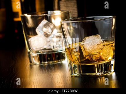 bicchiere di whisky con ghiaccio davanti al bicchiere vuoto sul tavolo di legno Foto Stock