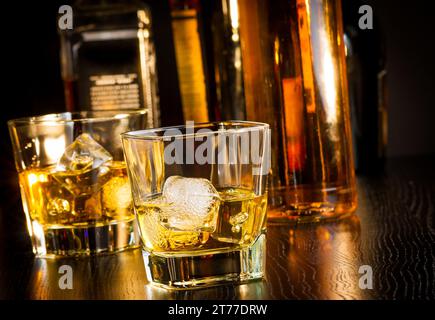 due bicchieri di whisky davanti alle bottiglie sul tavolo di legno Foto Stock