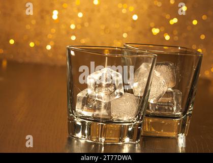 due bicchieri da whisky vuoti su tavola di legno e sfondo bokeh dorato Foto Stock