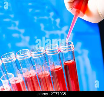 primo piano delle provette con pipetta su liquido rosso su sfondo di laboratorio sfocato Foto Stock