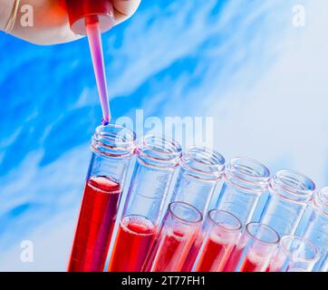 primo piano delle provette con pipetta su liquido rosso su sfondo astratto blu Foto Stock