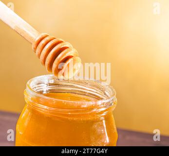 vaso di miele aperto su tavolo in legno con cucchiaia in legno sulla parte superiore con miele a goccia su fondo dorato Foto Stock