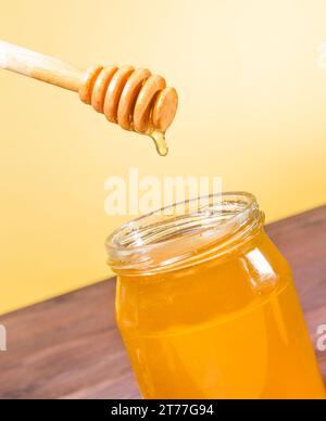 vasetto di miele aperto su tavola di legno con sommità di miele in legno e miele goccia su fondo dorato Foto Stock