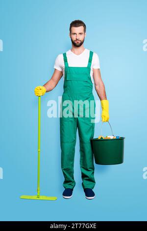 Ritratto integrale di bella e attraente governante con stoppia, acconciatura in uniforme verde, isolato su sfondo grigio, con secchio Foto Stock