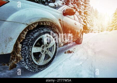 Primo piano grandangolare di un'auto piena di neve in inverno, su una strada di montagna con il tramonto alle spalle Foto Stock