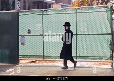 Un ebreo ortodosso cammina davanti a un cantiere edile in una fredda giornata autunnale nel 2023. A Williamsburg, Brooklyn, New York. Foto Stock