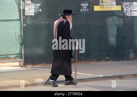 Un anziano ebreo ortodosso con una lunga barba bianca cammina tra le grondaie davanti a un cantiere edile. A Williamsburg, Brooklyn, New York. Foto Stock