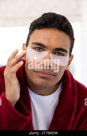 Felice uomo birazziale che applica cerotti uder-eye in bagno a casa Foto Stock