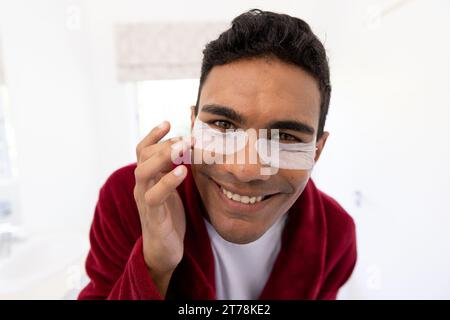 Felice uomo birazziale che applica cerotti uder-eye in bagno a casa Foto Stock