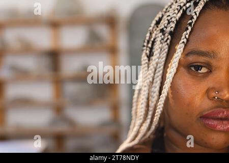 Mezzo volto di una seria ceramista afroamericana con trecce in piedi in uno studio di ceramica Foto Stock