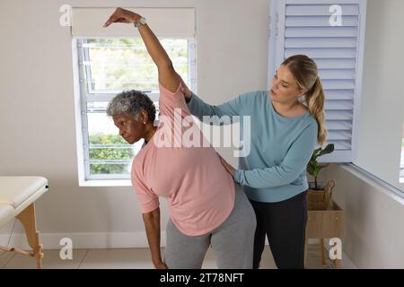 Fisioterapista femminile caucasica e paziente afrcia americana anziana che si allunga, spazio di copia Foto Stock