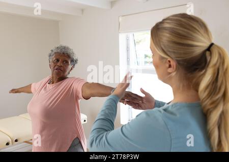 Fisioterapista femminile caucasica e paziente afrcia americana anziana che si allunga, spazio di copia Foto Stock