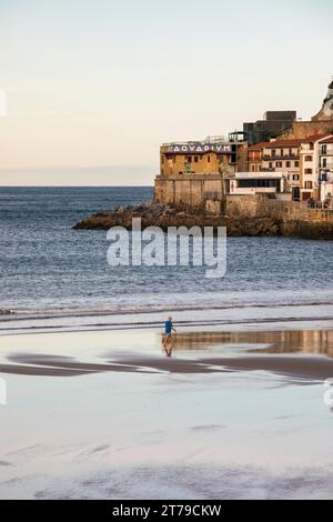 Uomo che cammina lungo il Bahía de la Concha a San Sebastián con la bassa marea al mattino. Foto Stock
