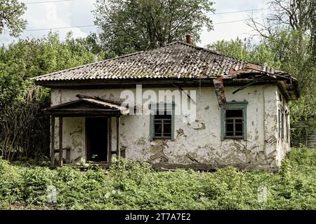 Una foto di una vecchia casa fatiscente con un tetto in rovina e una vegetazione straripata. Foto Stock