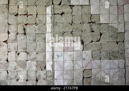 Una parete intemprata con uno schema a zigzag, che mostra segni di decadimento e danni. Il vecchio muro con cui le piastrelle frontali crollavano. Contesto. Foto Stock
