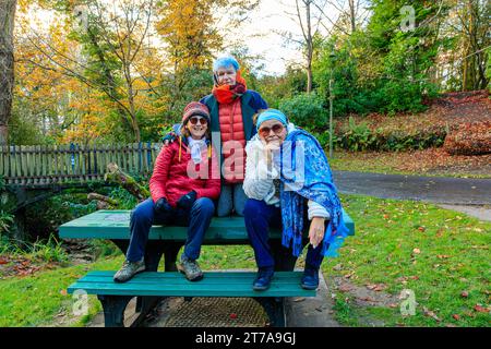 3 donne anziane oltre i 60 anni si rilassano sedute sulla panchina dopo una passeggiata nel parco il giorno autunnale all'Hermitage Park, Helensburgh, Argyll e Bute, Scozia Foto Stock