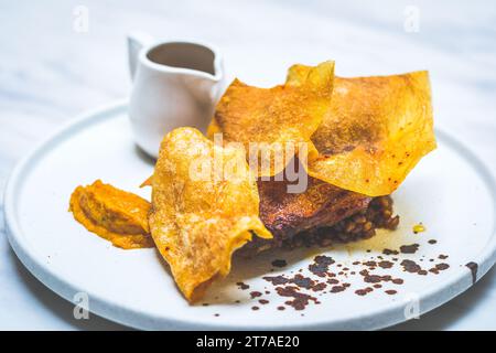 48 ore di confit di gambe di anatra essiccate all'aria, glassa di miele piccante, fogli di patate, fricasse di farro e funghi, jus tamarindo Foto Stock