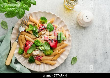 Penne per pasta integrale con broccoli e peperone rosso grigliato e su sfondo grigio chiaro ardesia, pietra o cemento. Pasta vegana. Tradizionale Itali Foto Stock