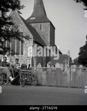 Anni '1950, storico, tre giovani, adolescenti più grandi - primi anni '20 in vacanza insieme, fuori dalla chiesa di St Mary a Hayling Island, Hampshire, Inghilterra, Regno Unito. Due dei ragazzi sono seduti su una bicicletta da campeggio a due posti, a quattro ruote, dice. "Higworth Farm Caravan Camp", un popolare luogo di vacanza nel sud-est dell'Inghilterra per le famiglie che lavorano in questa epoca. Foto Stock