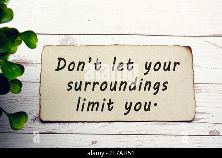 Citazione motivazionale e stimolante su carta marrone bruciata su una scrivania in legno - non lasciate che l'ambiente circostante vi limiti. Foto Stock