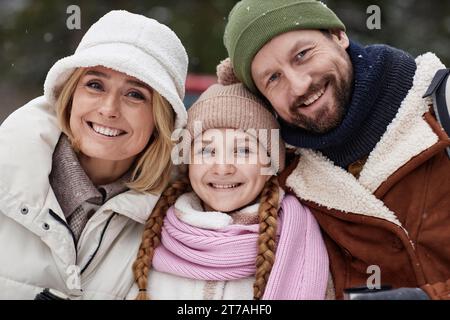 Ritratto di una famiglia felice di tre persone in inverno, con cappotti e berretti che guardano la macchina fotografica con sorrisi, mentre vi godete una gita nel fine settimana o un'escursione nella foresta Foto Stock