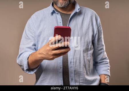 Un uomo di mezza età è impegnato con uno smartphone, catturando l'essenza della comunicazione moderna, l'integrazione tecnologica nella vita quotidiana e l'intersezione Foto Stock