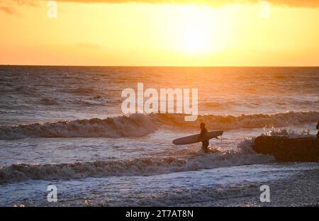 Brighton Regno Unito 14 novembre 2023 - Un surfista entra in mare a Brighton al tramonto dopo una giornata di sole e docce lungo la costa meridionale: Credit Simon Dack / Alamy Live News Foto Stock