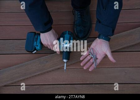 Costruzione di carpenteria ponte in legno, installazione di ponti falegname mani che tengono attrezzi da lavoro, cacciavite elettrico e viti Foto Stock