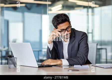 Lavoratore d'ufficio stanco seduto alla scrivania di fronte al computer portatile, stanco per un sacco di lavoro, esaurimento, mal di testa. Foto Stock