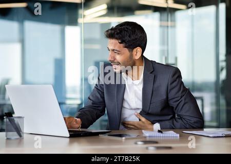 Operaio arabo malato. Dolore allo stomaco, sensazione di crampi allo stomaco durante il lavoro con un notebook, costipazione o bruciore di stomaco. Disagio acuto, problemi digestivi, dolore addominale acuto. Sensazione spiacevole. Foto Stock