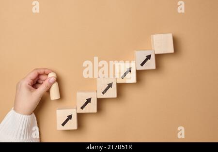 Gradini di legno e una figurina di un piccolo uomo in mano di una donna. Avvio, avvio di un nuovo business di successo, raggiungimento degli obiettivi Foto Stock