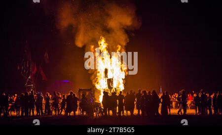 Un gruppo di persone si riunisce intorno a un falò caldo e ardente la sera, godendosi la luce ambientale e l'aria aperta Foto Stock