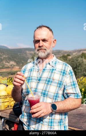 Uomo barbuto in camicia estiva a quadri che beve succo al mercato o bazar durante la sua vacanza Lifestyle Concept tempo libero in pensione Foto Stock