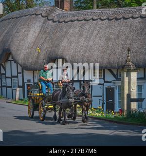 Cavallo e carretto di fronte ai tradizionali cottage in legno incorniciati in paglia a Church Street, Wherwell, Hampshire, Inghilterra, Regno Unito Foto Stock