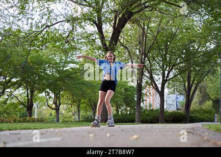 Giovane donna che pattina su pattini in linea nel parco a braccia aperte, donna caucasica che si diverte mentre fa sport nelle sue attività ricreative. Foto Stock