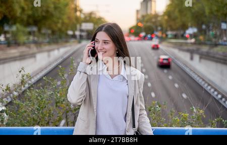 giovane donna in blazer che parla al cellulare Foto Stock