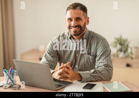 uomo di mezza età sorridente mentre lavora su un notebook in ufficio Foto Stock