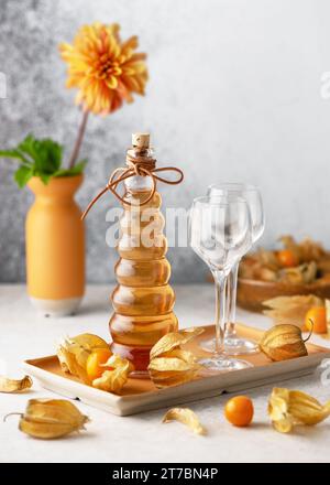 Deliziosa bevanda rinfrescante sana, sciroppo di bacche dorate o cordiali in una bottiglia di vetro su un vassoio con frutta fresca di Physalis. Concetto di cibo fatto in casa. Foto Stock