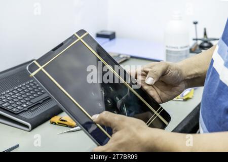 Un tecnico che ripara lo schermo di un tablet grande e sottile nella sua officina di elettronica Foto Stock