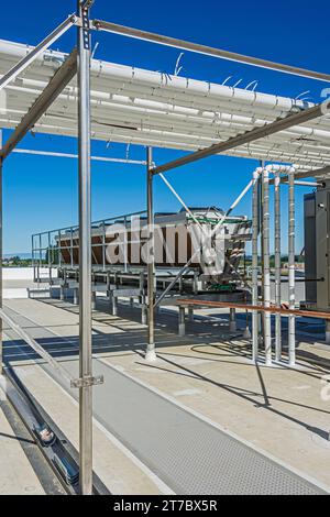 Uno sguardo attraverso un telaio di supporto per tubi verso un condensatore adiabatico sul tetto di un magazzino di stoccaggio a freddo di CO2 (refrigerazione industriale) Foto Stock