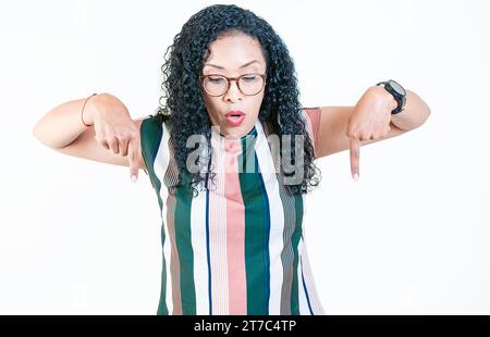 Sorpreso la giovane donna afro che punta a fare pubblicità isolata. Scioccata donna latina che punta e guarda in basso Foto Stock