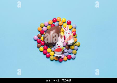 Due coniglietti bianchi con uova di pasqua colorate caramelle su sfondo blu Foto Stock