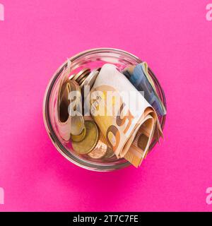 Vista dall'alto banconote in euro le monete aprono il vaso di vetro su sfondo rosa Foto Stock