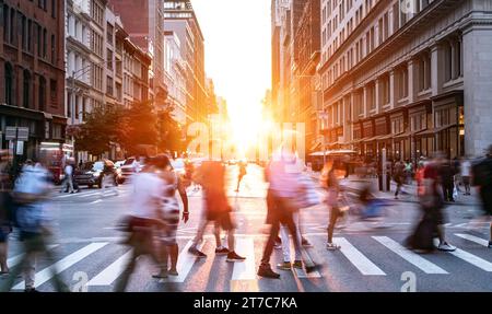 Folle di persone che camminano attraverso l'intersezione tra la 5th Avenue e la 23rd Street a New York City con la luce del tramonto che splende sullo sfondo Foto Stock